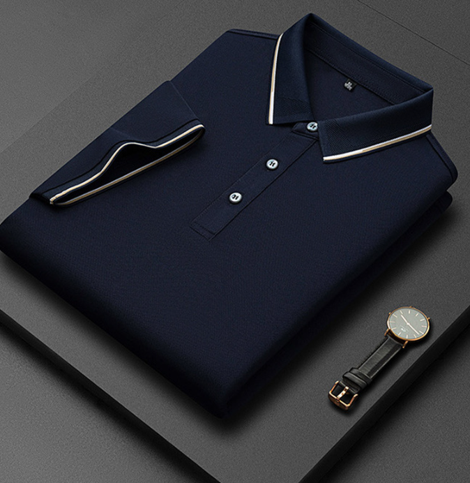 Camicia polo blu scuro piegata con colletto a contrasto, abbinata a un elegante orologio da polso nero su sfondo grigio. Moda uomo, abbigliamento casual.