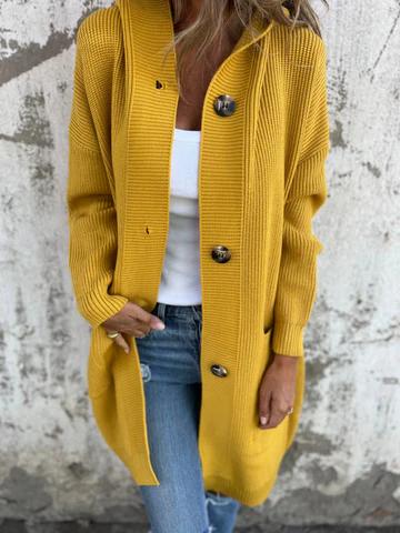 Donna con cardigan giallo a maglia grossa, bottoni grandi, indossa jeans blu e top bianco. Moda autunnale casual, stile urbano.