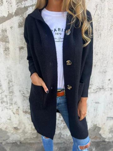 Donna con cardigan nero lungo, bottoni grandi, tasche frontali, indossa jeans strappati e maglietta bianca. Moda casual autunnale.