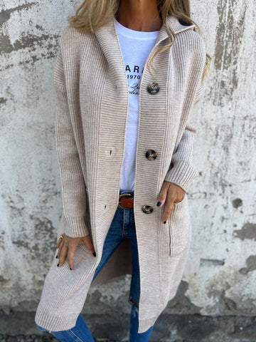 Donna con cardigan beige a coste, bottoni grandi, su sfondo muro grigio. Moda autunnale, abbigliamento casual, stile urbano.