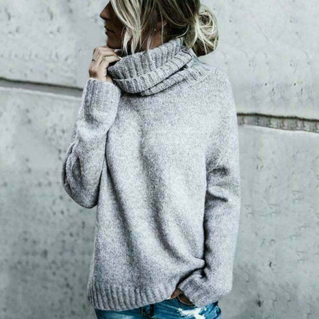 Donna con maglione grigio a collo alto, stile casual, posa contro muro di cemento. Moda autunno inverno, abbigliamento caldo e confortevole.