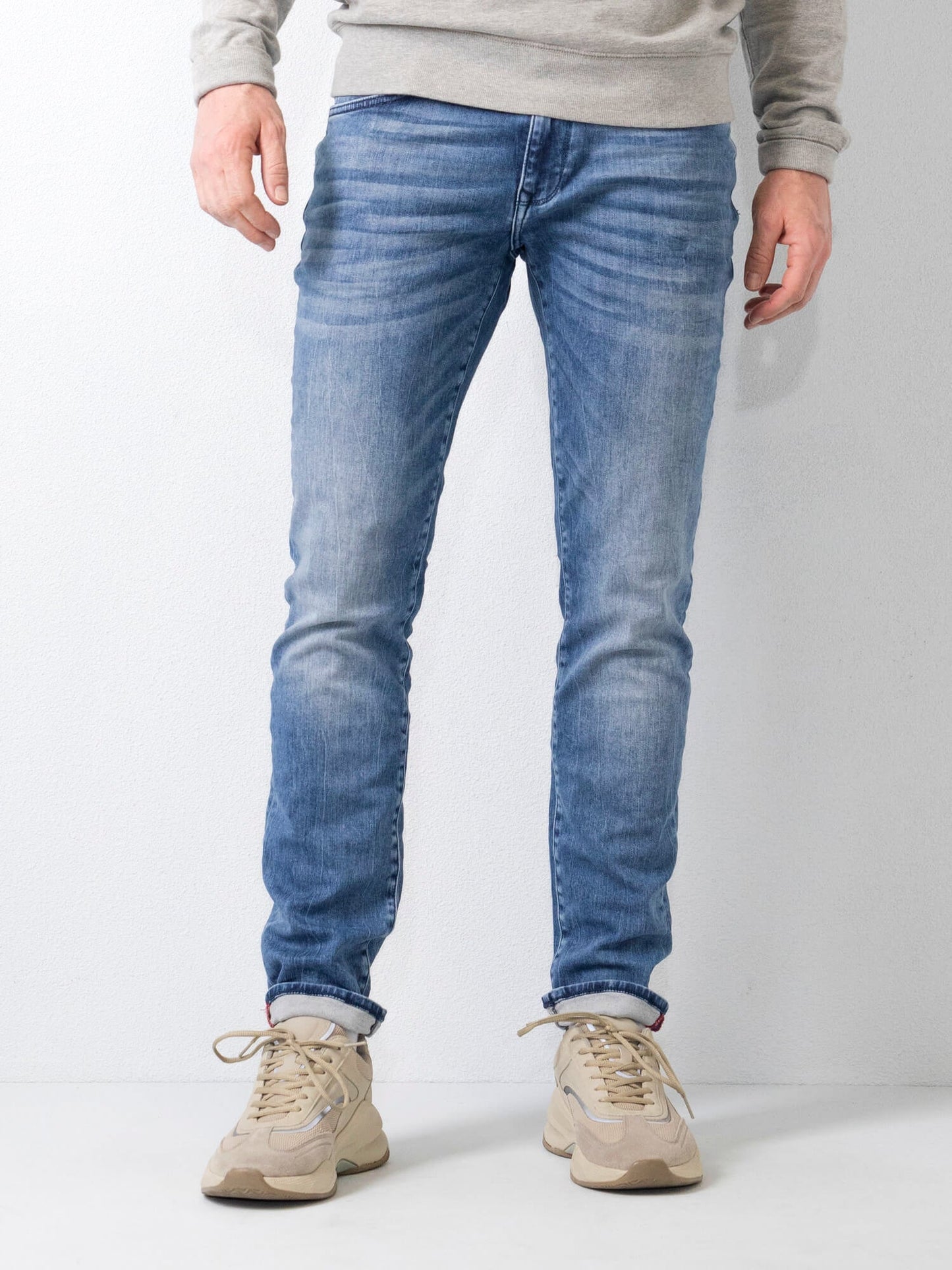 Jeans slim fit uomo in denim blu chiaro, abbinati a scarpe sportive beige, su sfondo bianco. Moda casual maschile, abbigliamento trendy.