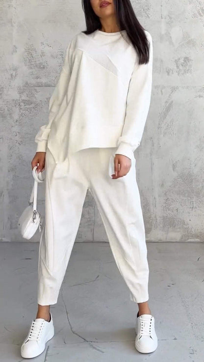 Donna in abbigliamento casual bianco, con maglione e pantaloni coordinati, borsa a tracolla e scarpe da ginnastica, su sfondo grigio.