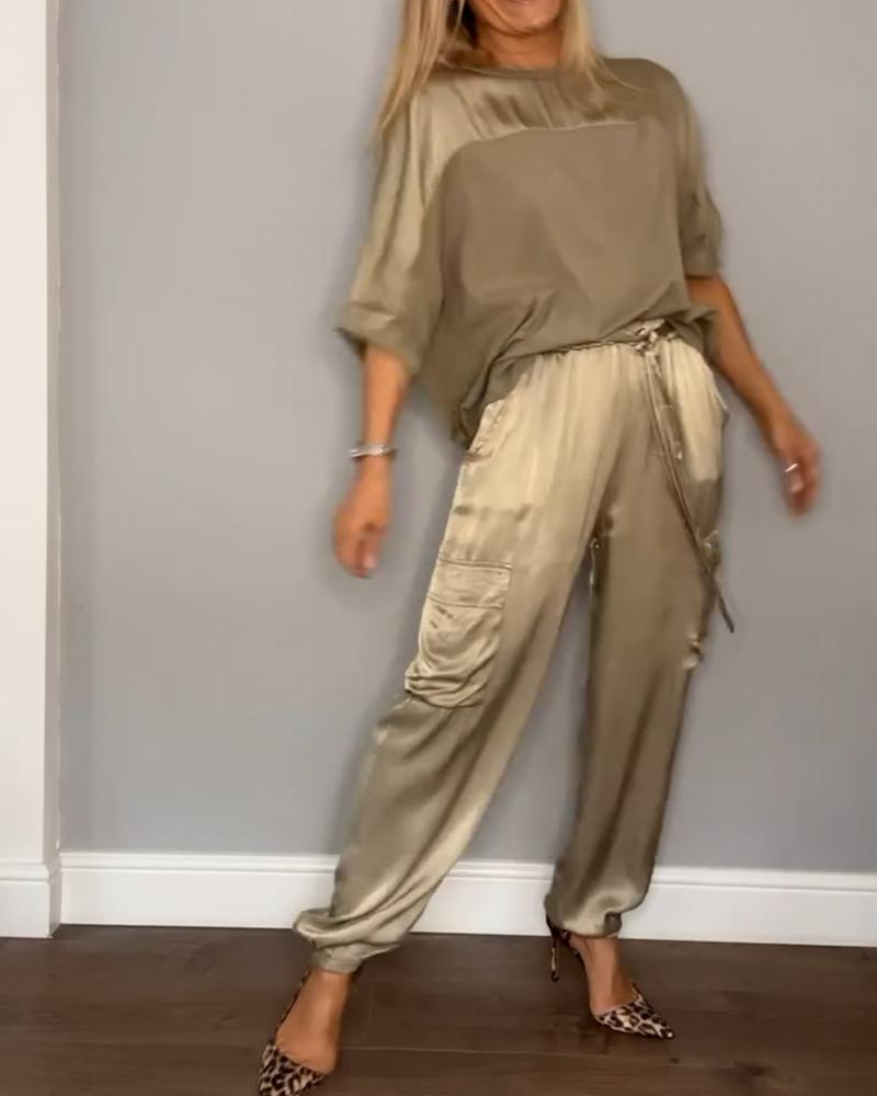 Donna in abbigliamento elegante color oro, indossa pantaloni cargo satinati e blusa coordinata, con tacchi leopardati. Moda femminile chic.