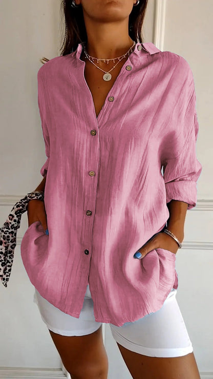 Camicia rosa in lino con bottoni, maniche lunghe arrotolate, indossata con pantaloni bianchi. Stile casual elegante, moda donna primavera estate.