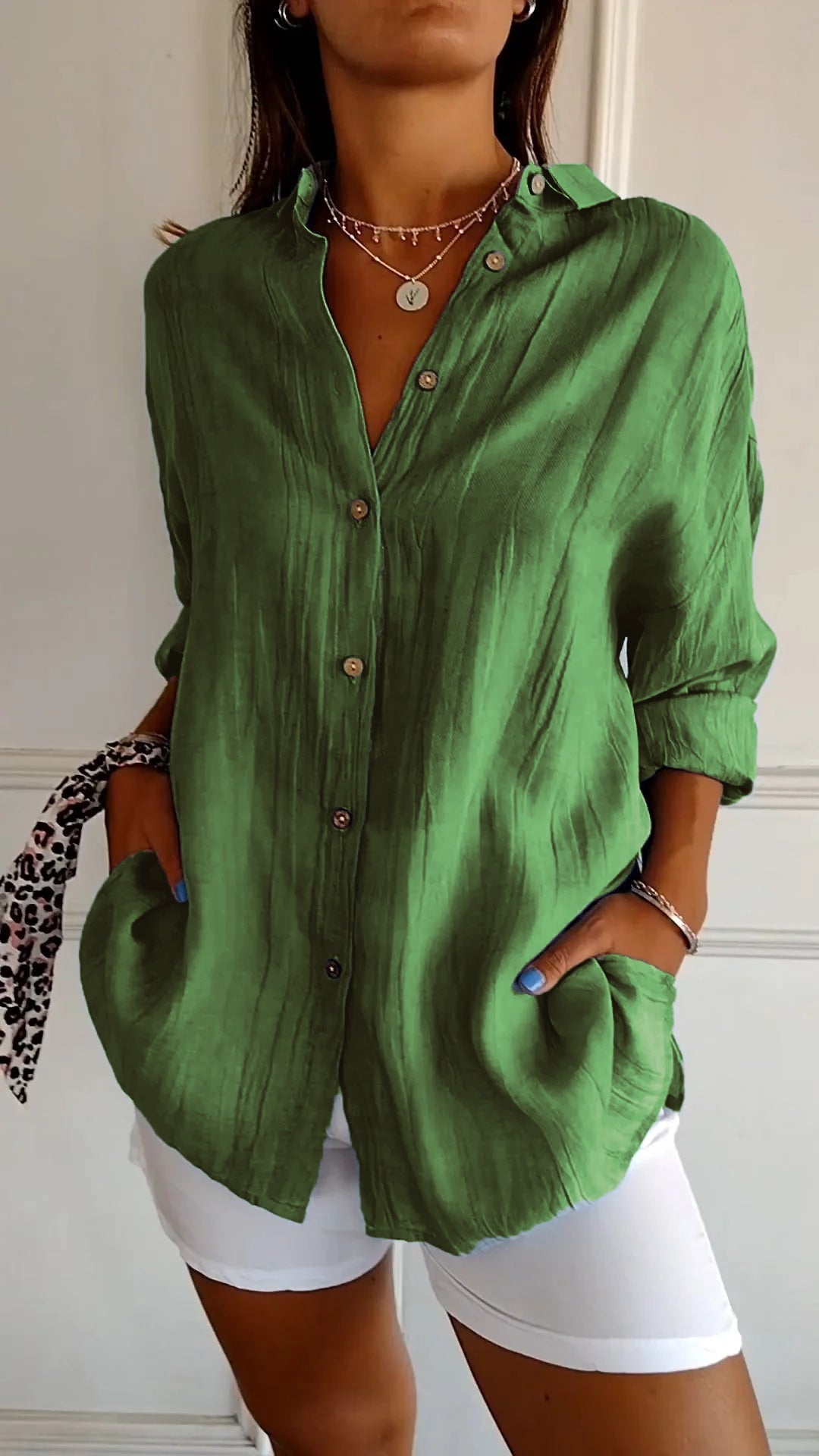 Camicia verde in lino con bottoni, maniche lunghe arrotolate, abbinata a pantaloni bianchi. Stile casual chic, moda donna estiva.