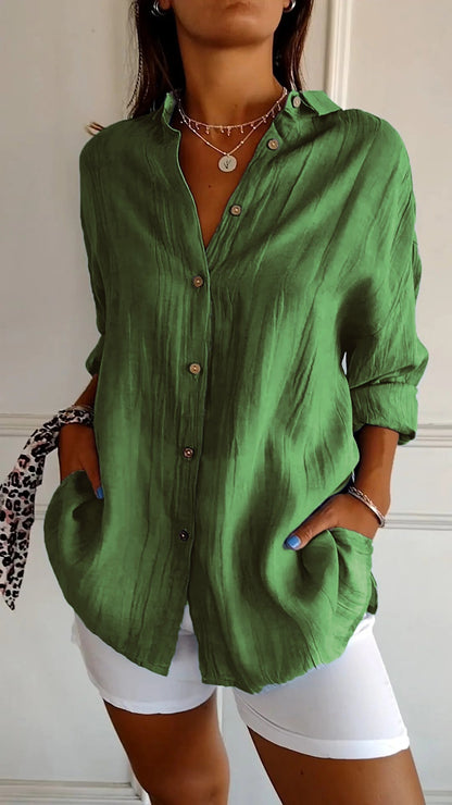 Camicia verde in lino con bottoni, maniche lunghe arrotolate, abbinata a pantaloni bianchi. Stile casual chic, moda donna estiva.