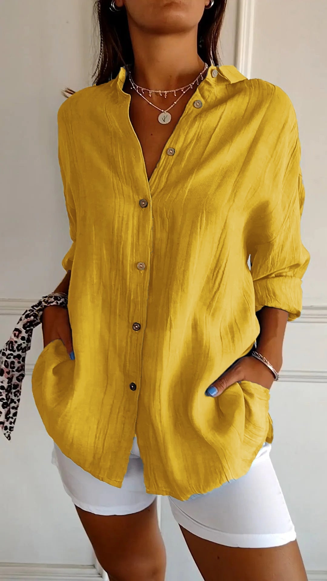 Camicia gialla in lino con bottoni, maniche lunghe arrotolate, indossata con pantaloni bianchi. Stile casual elegante, moda donna estiva.