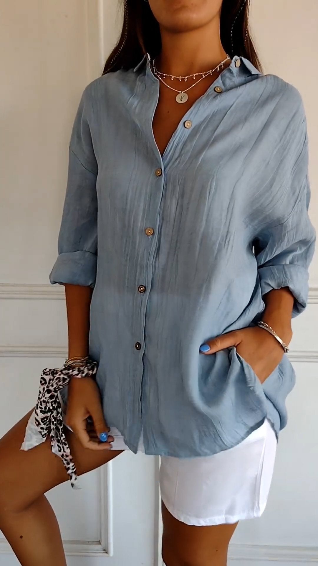 Camicia donna azzurra in lino con bottoni, maniche arrotolate, abbinata a pantaloncini bianchi. Look estivo casual chic.