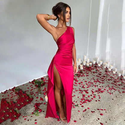 Donna in abito rosso elegante con spacco alto, circondata da petali di rosa e candele, posa in un ambiente romantico. Moda, abbigliamento da sera.