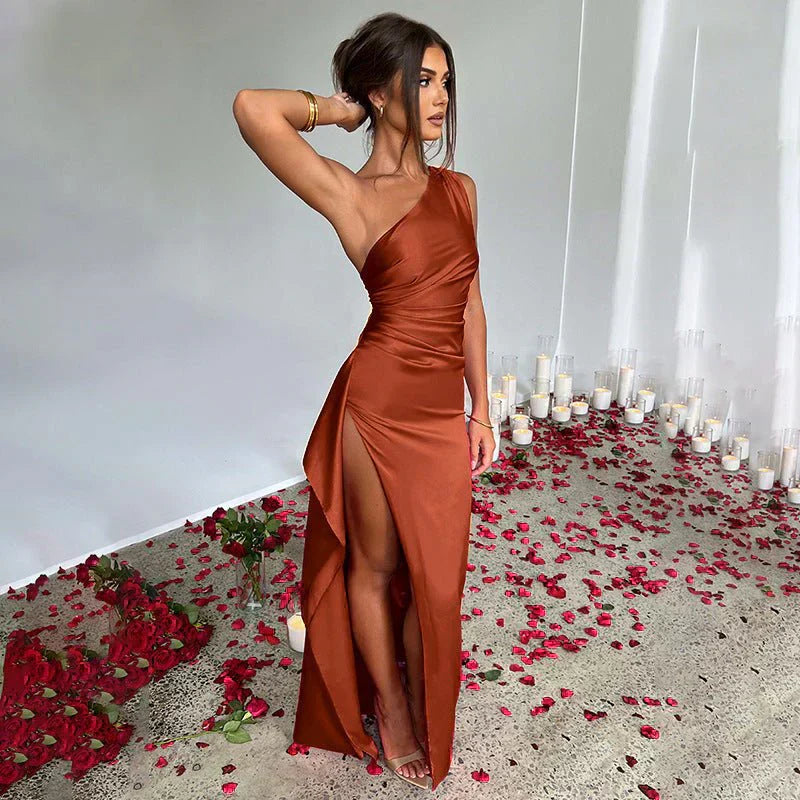 Donna in abito lungo arancione con spacco, circondata da petali di rosa rossi e candele, posa in un ambiente elegante. Moda, eleganza, serata.