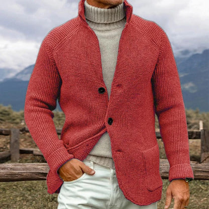 Giacca cardigan uomo rosso in maglia, abbinata a maglione grigio e pantaloni chiari, sfondo montagna. Moda autunnale casual elegante.