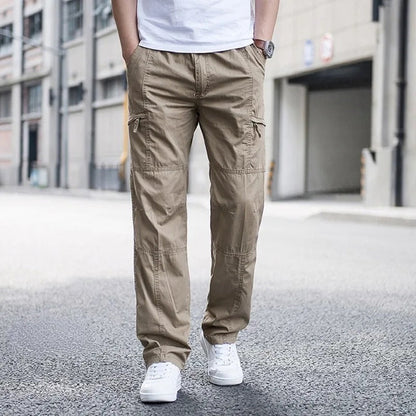 Pantaloni cargo beige da uomo, tasche multiple, indossati con scarpe bianche, sfondo urbano. Moda casual maschile, abbigliamento streetwear.