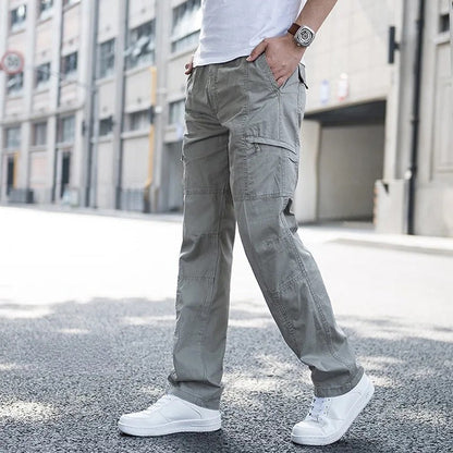 Uomo in pantaloni cargo grigi e scarpe da ginnastica bianche, cammina su strada urbana. Moda casual maschile, abbigliamento streetwear.