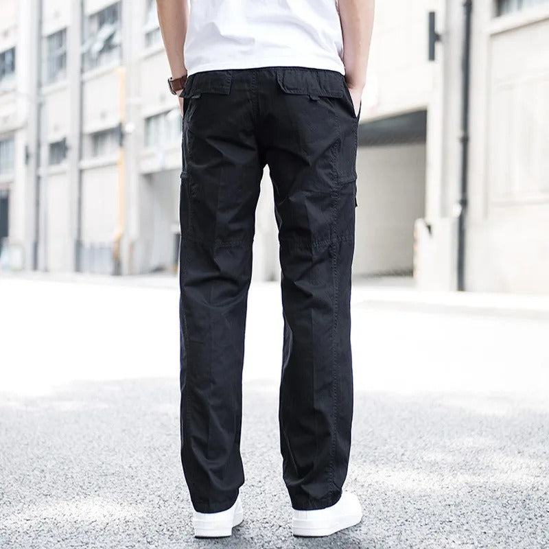 Pantaloni cargo neri da uomo, stile casual, indossati con scarpe bianche, sfondo urbano. Moda maschile, abbigliamento streetwear.