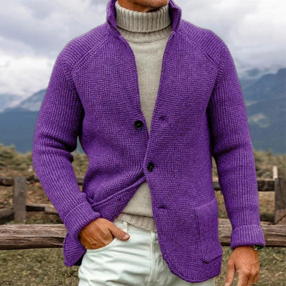 Uomo con maglione viola a maglia grossa e dolcevita beige, sfondo montano. Moda invernale, abbigliamento caldo, stile casual elegante.