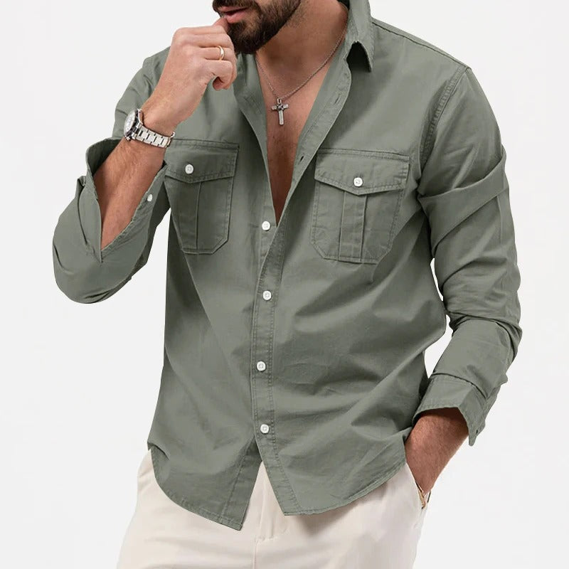Camicia verde militare da uomo con tasche frontali, maniche lunghe arrotolate, abbinata a pantaloni chiari. Stile casual elegante, moda maschile.