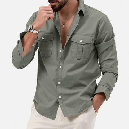 Camicia verde militare da uomo con tasche frontali, maniche lunghe arrotolate, abbinata a pantaloni chiari. Stile casual elegante, moda maschile.