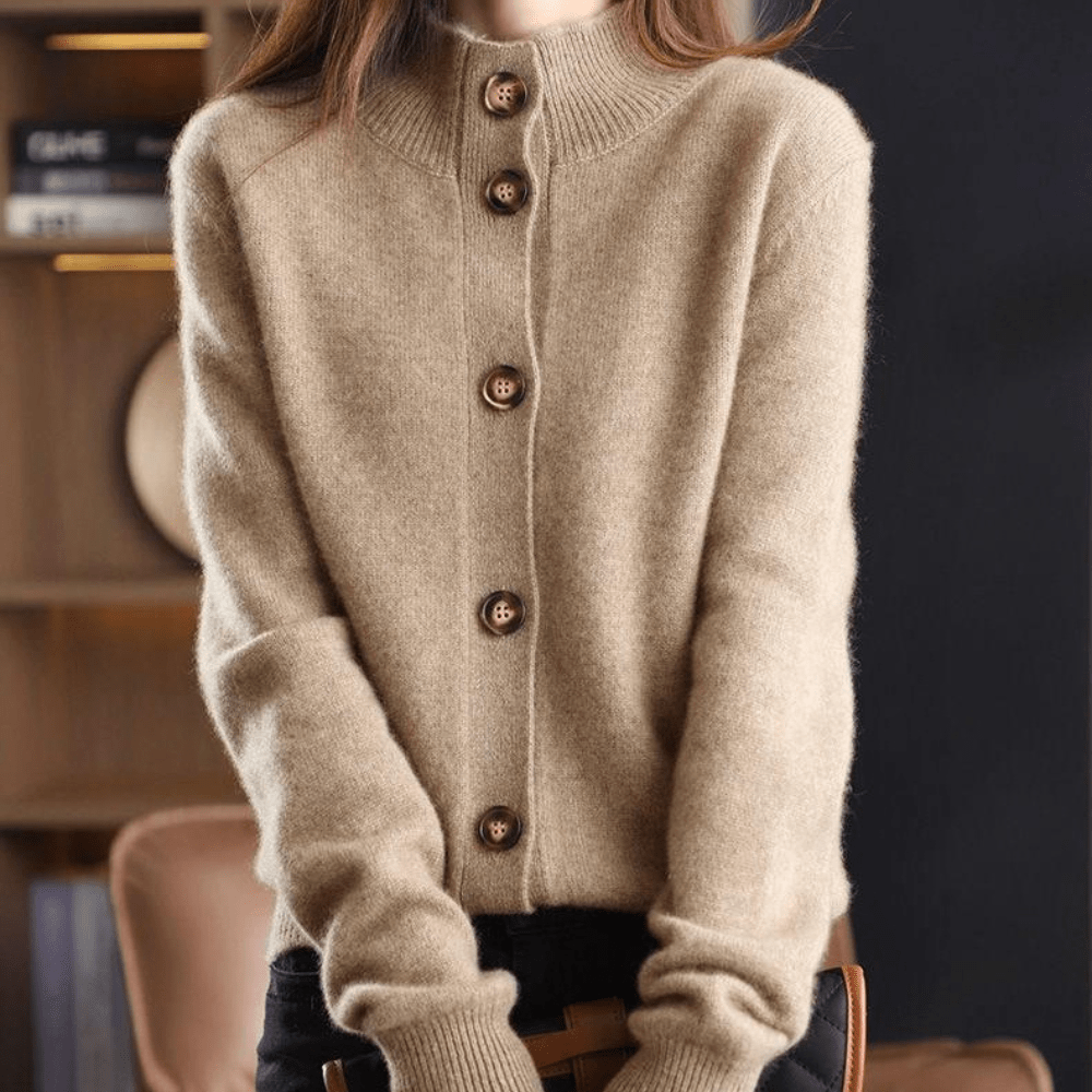 Maglione beige in cashmere con bottoni in legno, design a collo alto, indossato da una persona in un ambiente interno elegante.