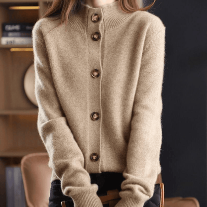 Maglione beige in cashmere con bottoni in legno, design a collo alto, indossato da una persona in un ambiente interno elegante.