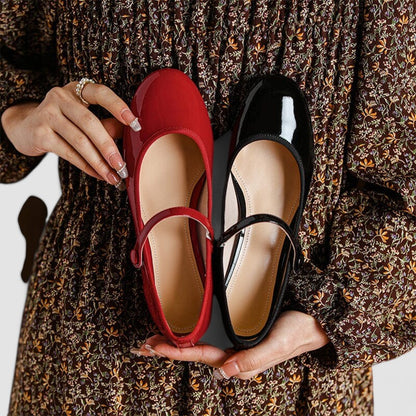 Donna con abito floreale tiene scarpe Mary Jane in vernice rossa e nera. Scarpe eleganti, moda femminile, calzature classiche.