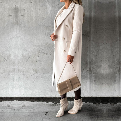 Donna in cappotto bianco elegante, stivali alla moda e borsa beige, posa contro parete grigia. Look autunnale chic e sofisticato.