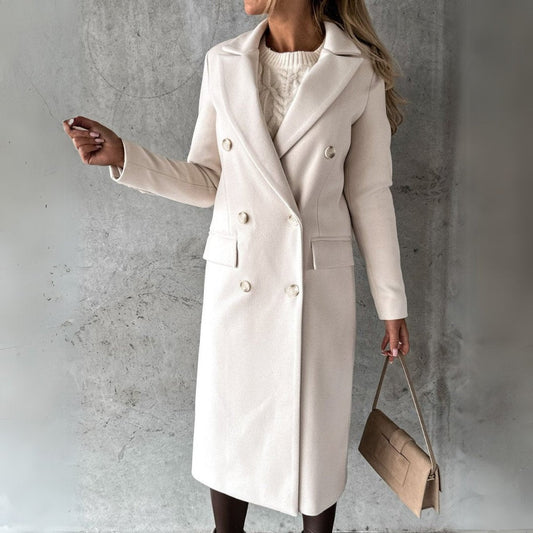 Donna con cappotto bianco elegante, doppio petto, in posa contro parete grigia. Moda autunno inverno, borsa beige, stile sofisticato.