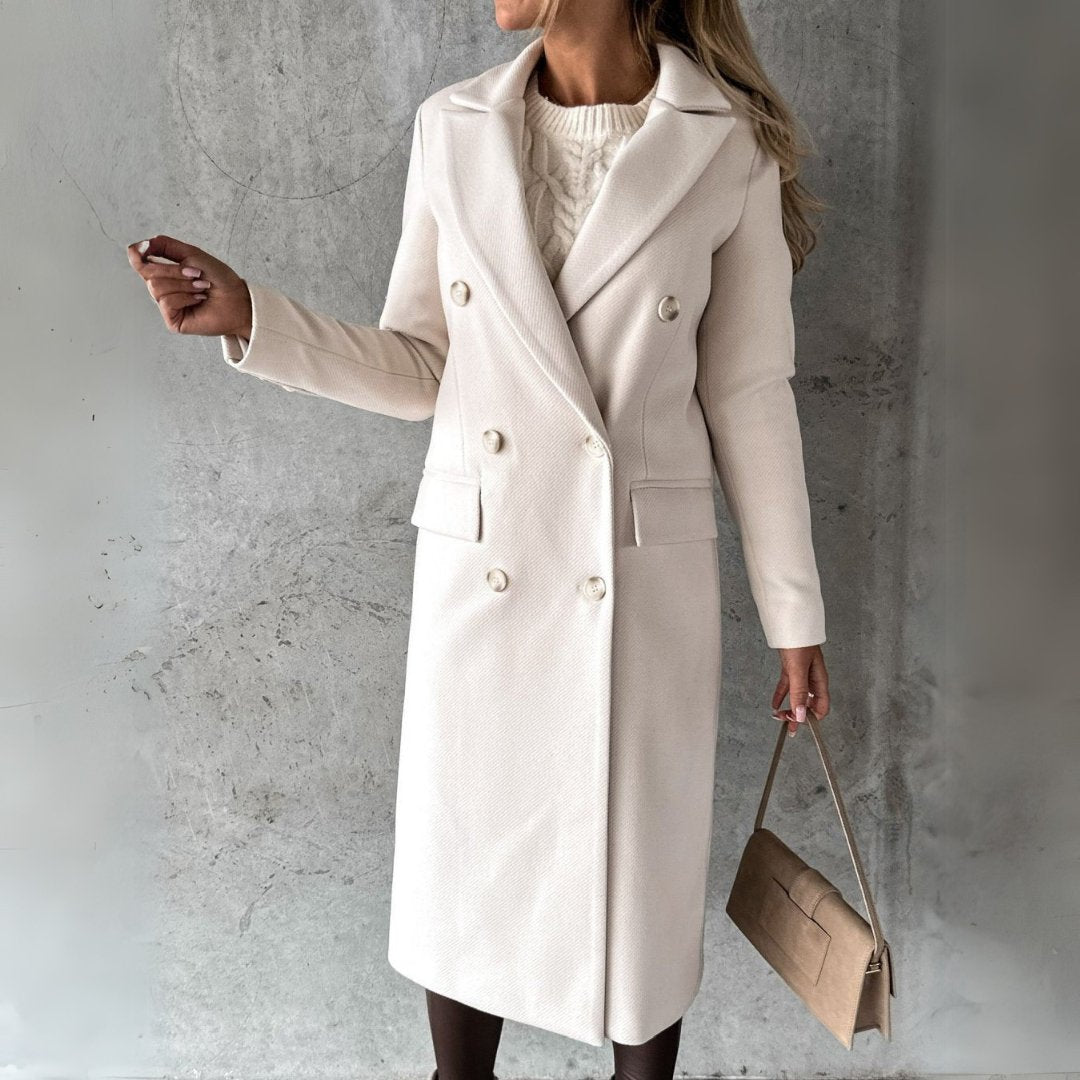 Donna con cappotto bianco elegante, doppio petto, in posa contro parete grigia. Moda autunnale, borsa beige, stile sofisticato.