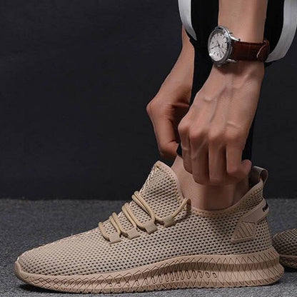 Scarpa sportiva beige con design a rete, suola antiscivolo e lacci, indossata da una persona con orologio al polso. Scarpe da ginnastica moderne.