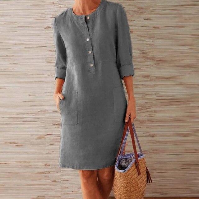Donna con abito grigio in lino, maniche lunghe, tasche frontali, tiene una borsa di paglia. Moda casual elegante, abbigliamento estivo femminile.