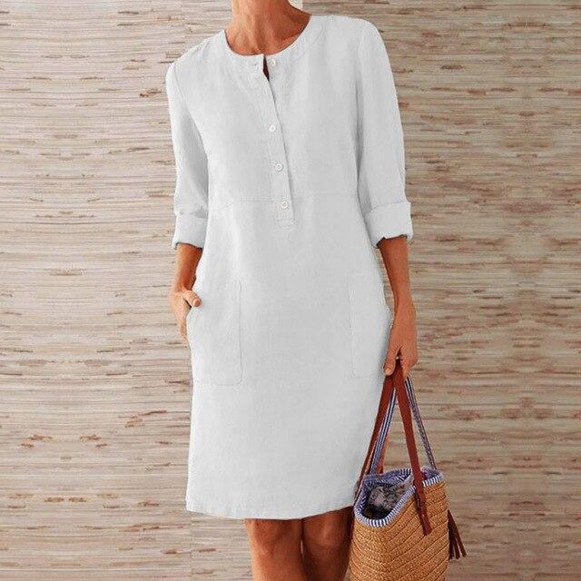 Donna con abito bianco casual a maniche lunghe, tasche frontali, tiene una borsa di paglia. Moda estiva, abbigliamento femminile elegante.