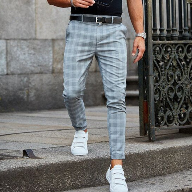 Uomo con pantaloni a quadri grigi e scarpe da ginnastica bianche, cammina su marciapiede di pietra. Moda maschile casual elegante.
