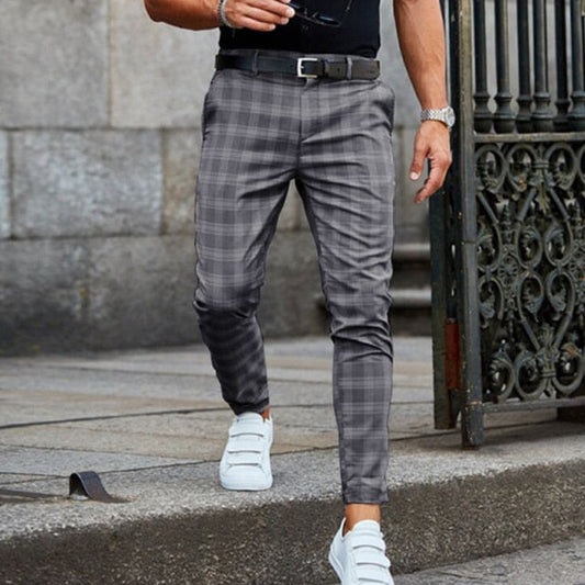 Uomo con pantaloni a quadri grigi e scarpe bianche cammina su marciapiede. Moda maschile elegante, look casual urbano.