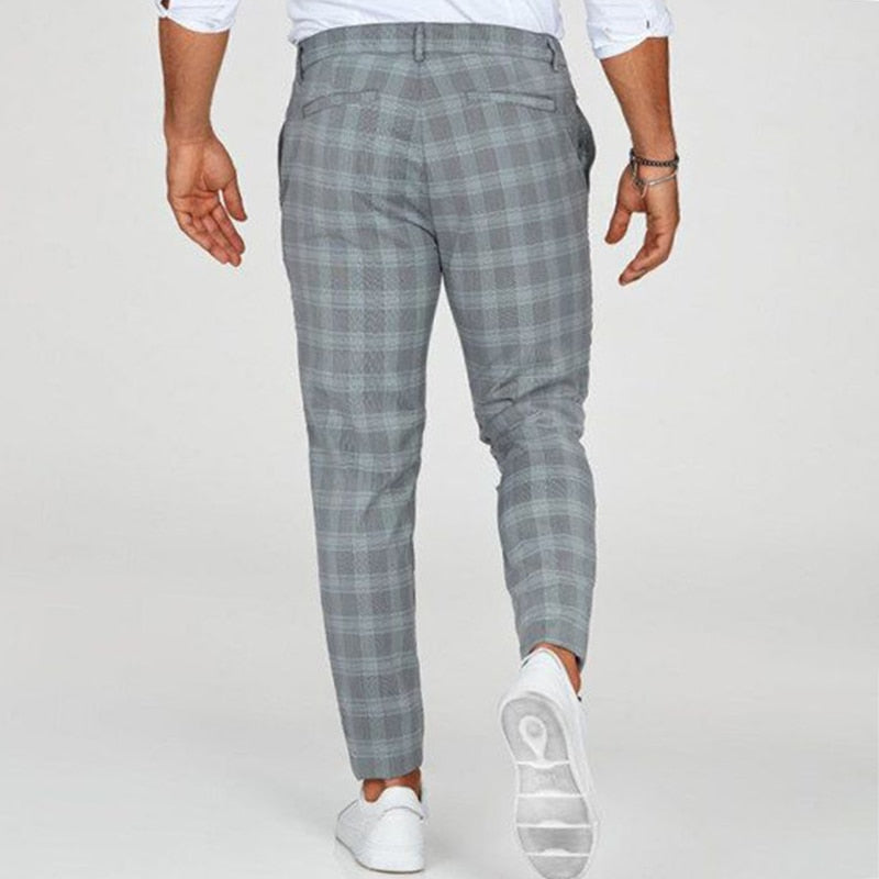 Uomo con pantaloni a quadri grigi, scarpe bianche, camicia bianca; moda maschile elegante, abbigliamento casual, stile moderno.