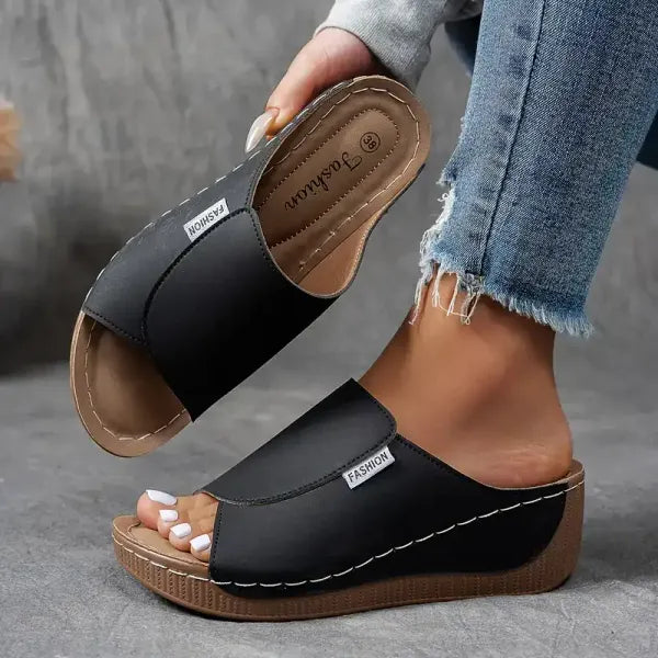 Sandali donna neri con zeppa, design aperto, etichetta "Fashion", indossati con jeans strappati. Calzature estive eleganti e comode.