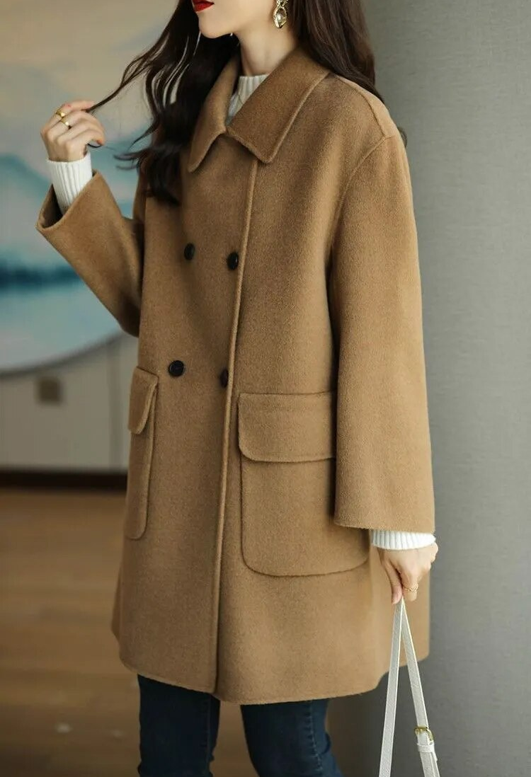 Cappotto donna invernale color cammello, doppio petto, tasche grandi, abbinato a maglione bianco e jeans. Elegante moda autunnale.