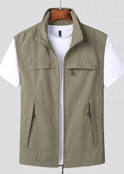 Gilet verde oliva da uomo con cerniera, tasche frontali, indossato sopra una maglietta bianca. Abbigliamento casual, moda maschile.