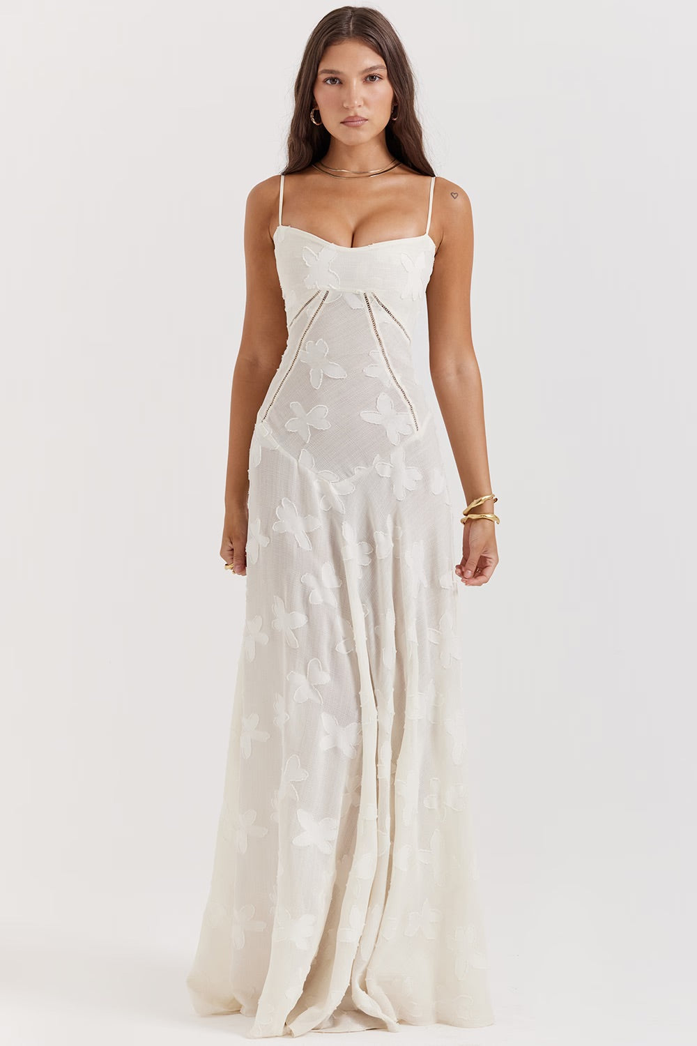Donna in abito lungo bianco con spalline sottili e motivo floreale, posa su sfondo neutro. Elegante vestito estivo, moda femminile.