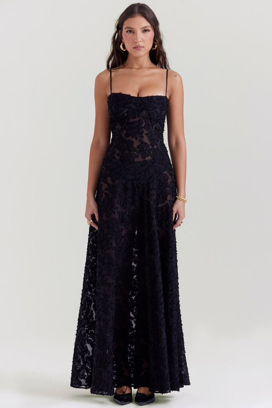 Donna in abito lungo nero trasparente con motivi floreali, spalline sottili, orecchini dorati e bracciale. Moda elegante, abbigliamento serale.