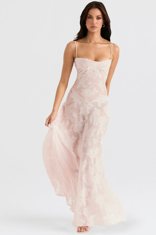 Donna in abito lungo rosa chiaro con spalline sottili e motivo floreale, elegante e sofisticato, ideale per eventi formali e cerimonie.