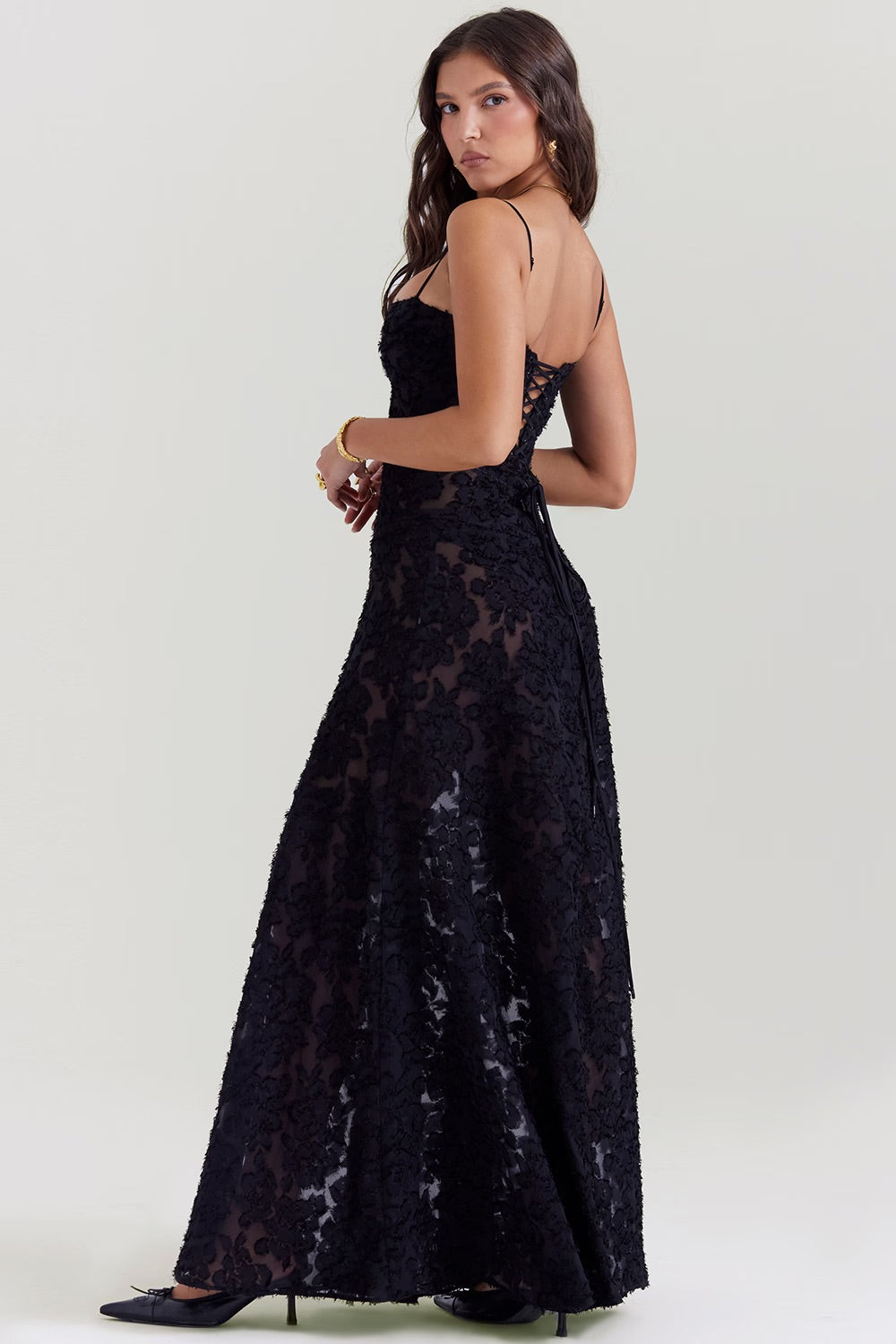 Donna in abito lungo nero elegante con dettagli in pizzo, spalline sottili e schiena scoperta. Moda serale, abbigliamento da cerimonia.