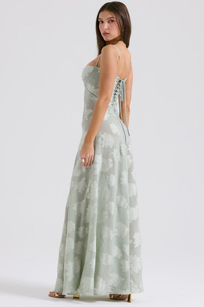 Donna in abito lungo verde chiaro con spalline sottili e motivo floreale, vista laterale. Elegante vestito estivo, moda femminile.