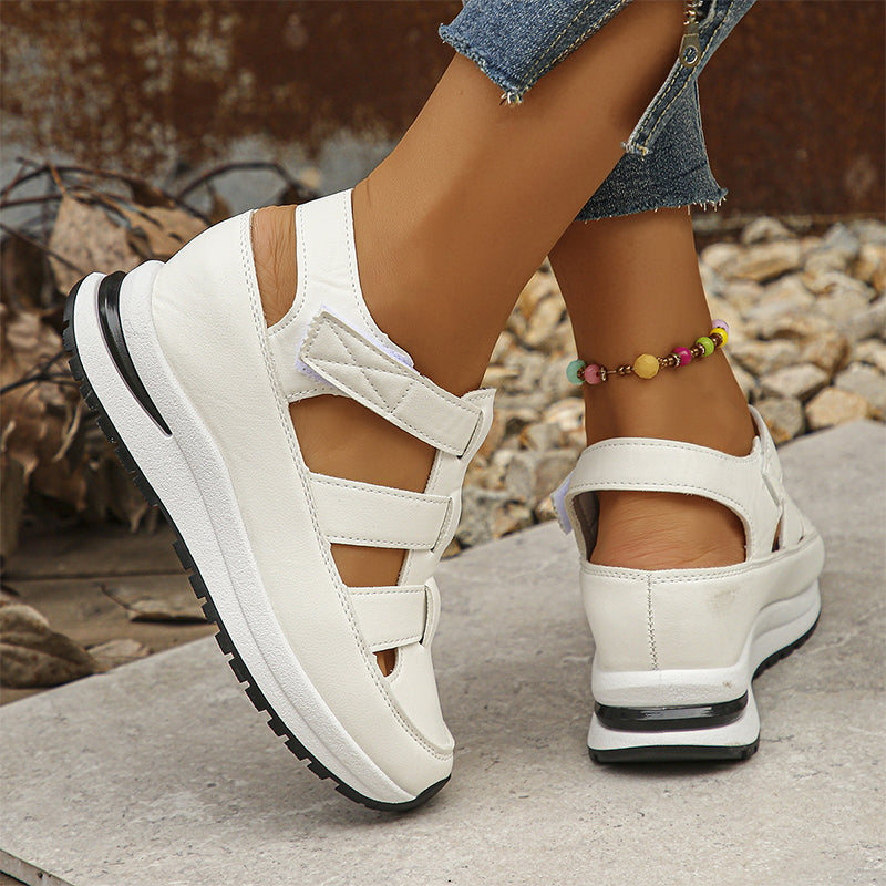 Scarpe da donna bianche con zeppa, design sportivo e cinturini, indossate con jeans e cavigliera colorata. Scarpe estive comode e alla moda.