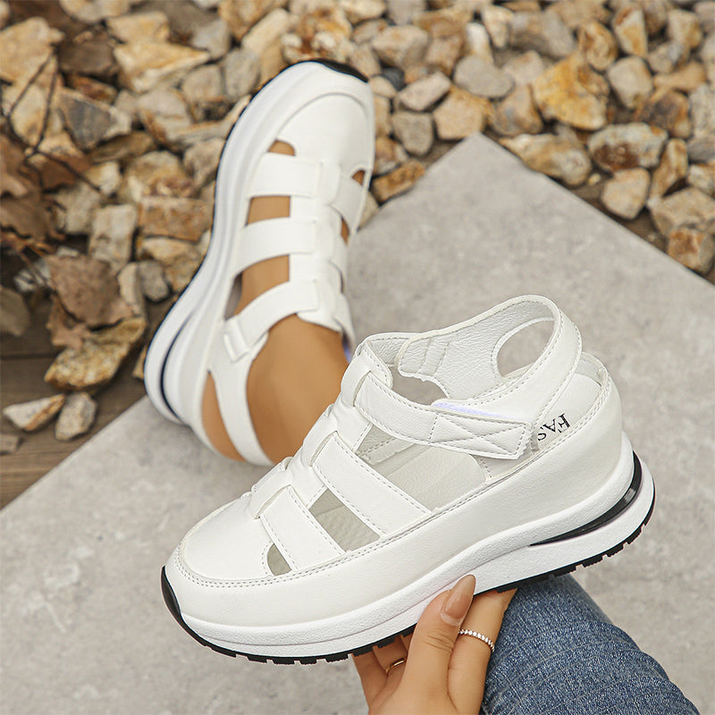 Sandali bianchi sportivi su suola spessa, indossati su sfondo di pietre. Design moderno e casual, perfetti per look estivi e passeggiate all'aperto.