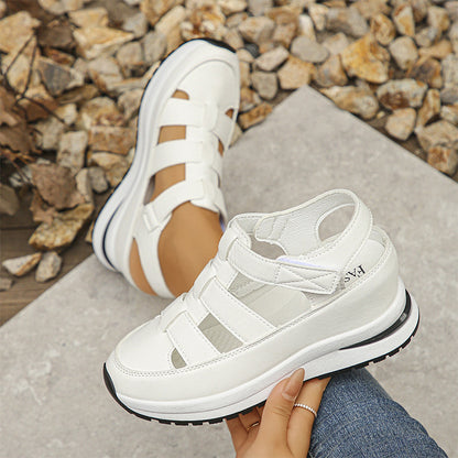 Sandali bianchi sportivi su suola spessa, indossati su sfondo di pietre. Design moderno e casual, perfetti per look estivi e passeggiate all'aperto.