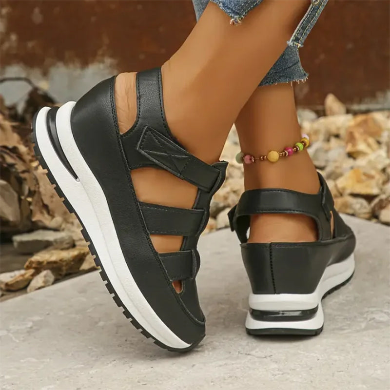 Scarpe da donna nere con zeppa, design sportivo e cinturini, indossate con jeans. Calzature estive eleganti e comode per passeggiate all'aperto.