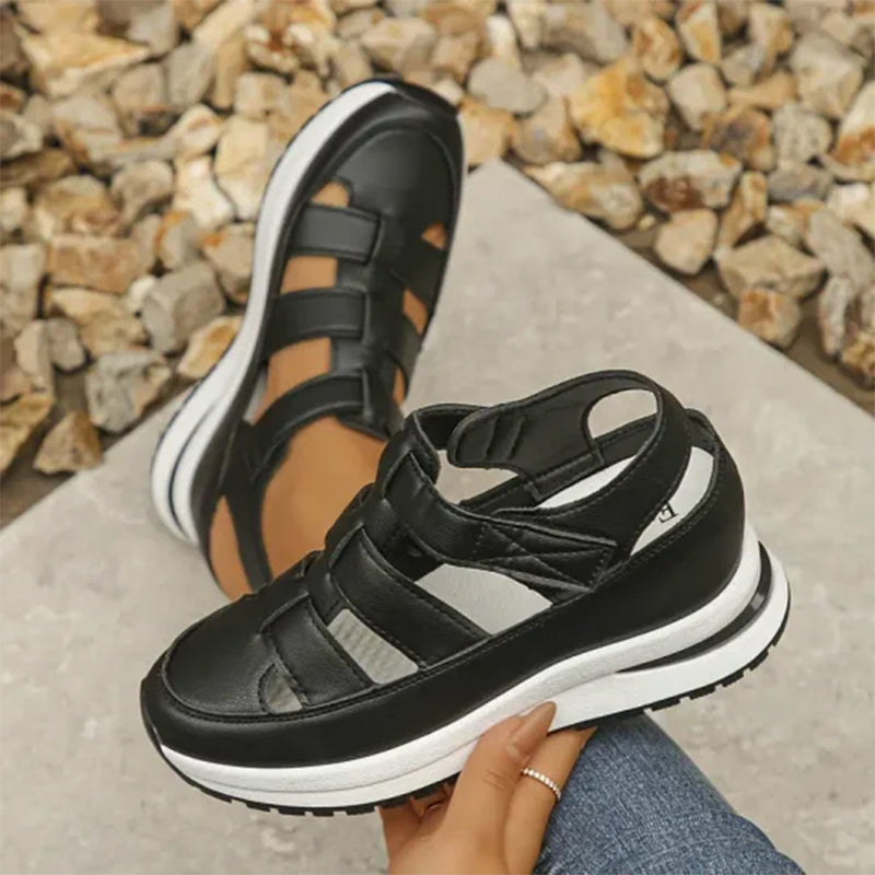 Sandali sportivi neri con suola spessa bianca, design a gabbia, indossati su sfondo di pietre. Scarpe estive comode e alla moda per donna.
