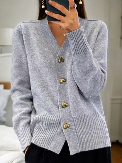 Donna con cardigan grigio in lana, bottoni a forma di cuore, stile casual elegante, moda autunnale, sfondo interno, accessori minimal.