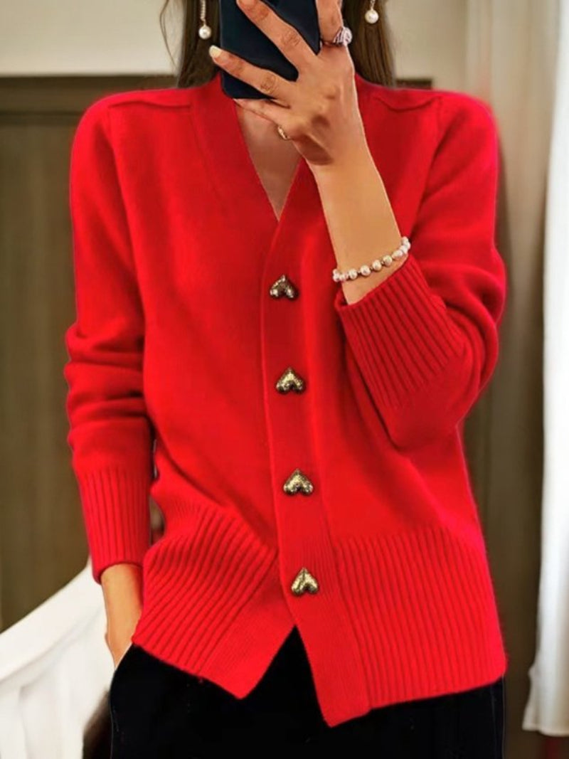 Donna con cardigan rosso acceso, bottoni a forma di cuore, maniche lunghe, indossa braccialetto di perle. Moda autunnale elegante e casual.