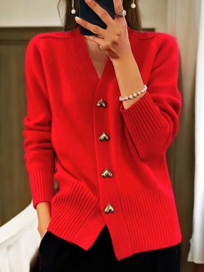 Donna con cardigan rosso acceso, bottoni a forma di cuore, maniche lunghe, indossa braccialetto di perle. Moda autunnale elegante e casual.